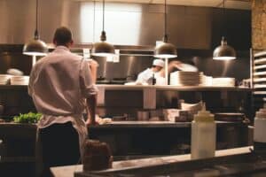 Chef preparing dishes in a busy restaurant kitchen, professional culinary team in action, modern commercial kitchen with stainless steel equipment and warm lighting, urban dining atmosphere, culinary arts, food safety, restaurant management, Spokane WA, Boyd Insurance coverage.