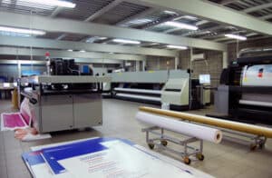 High-quality industrial printing and sign-making equipment in a commercial print shop, featuring large format printers and rollers, showcasing printing technology and signage production.