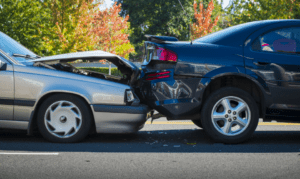Front-end collision between two cars on a road with autumn trees in the background.