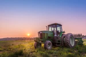 Green tractor on farmland at sunset, agricultural vehicle in Spokane WA for farm insurance and rural property coverage.